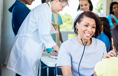 Nurse with a stethoscope talking with a patient with other medical workers in the background