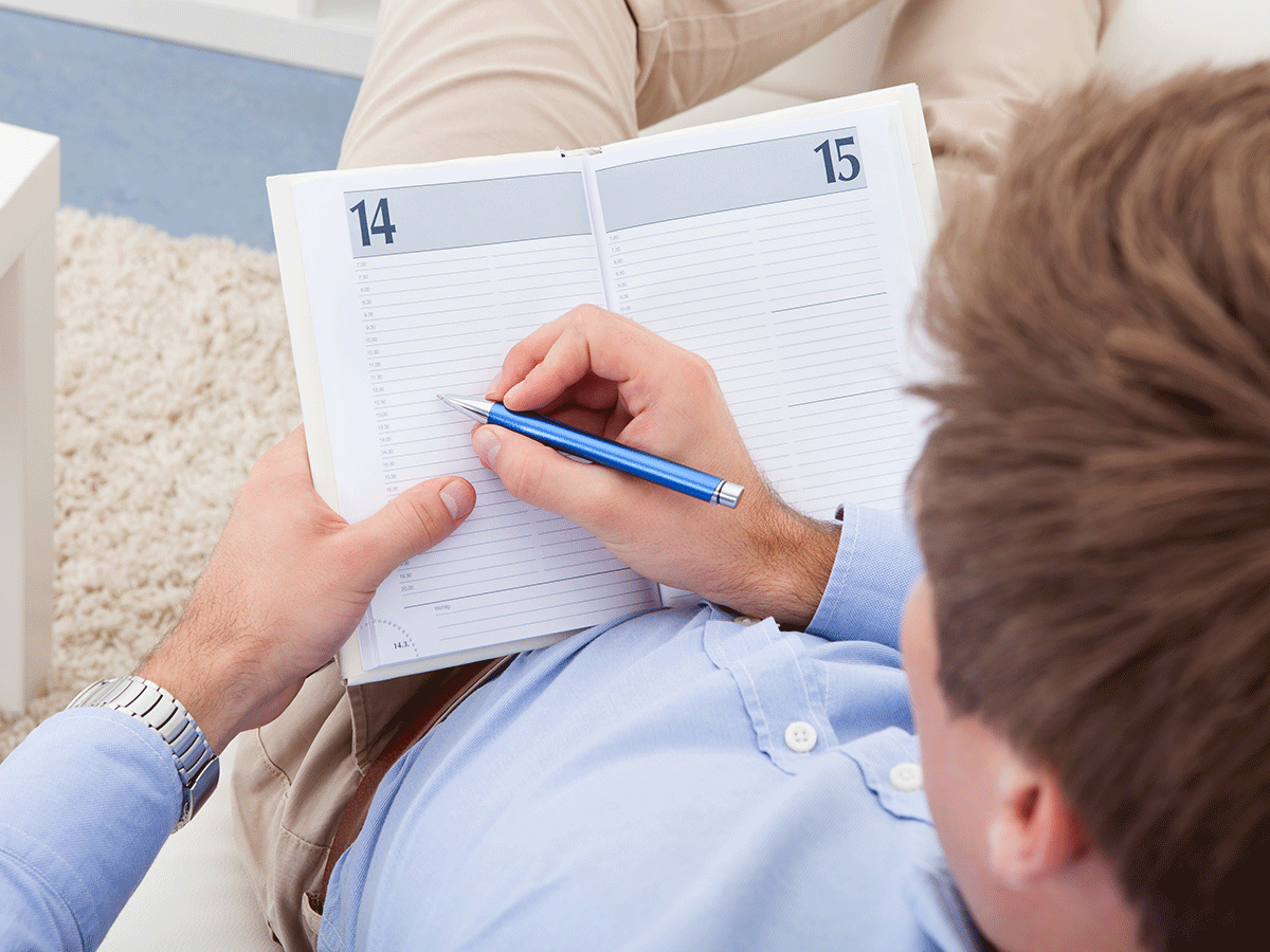 An overview image of a man writing into a calendar with a blue pencil